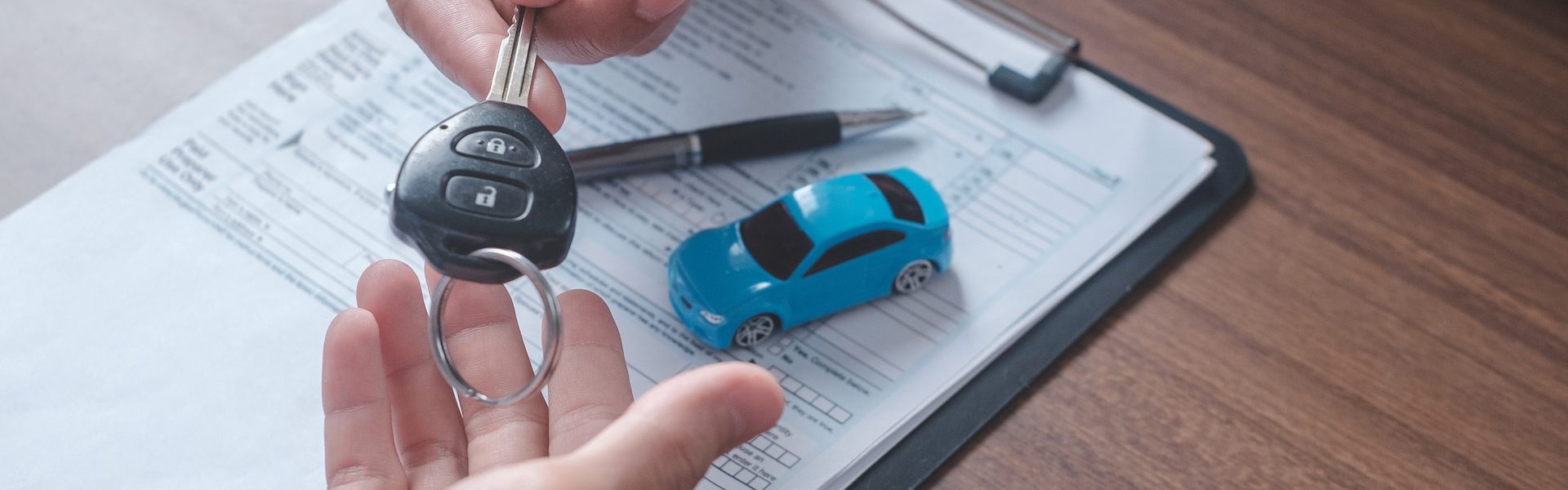 Concept car rental. Close up view Hand of agent giving car key to customer after signed rental contract form.